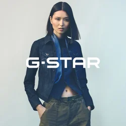 Giacca di jeans dal design aderente, colore blu scuro, con tasche sul davanti, abbinata a una camicia blu con bottoni e pantaloni verde oliva.