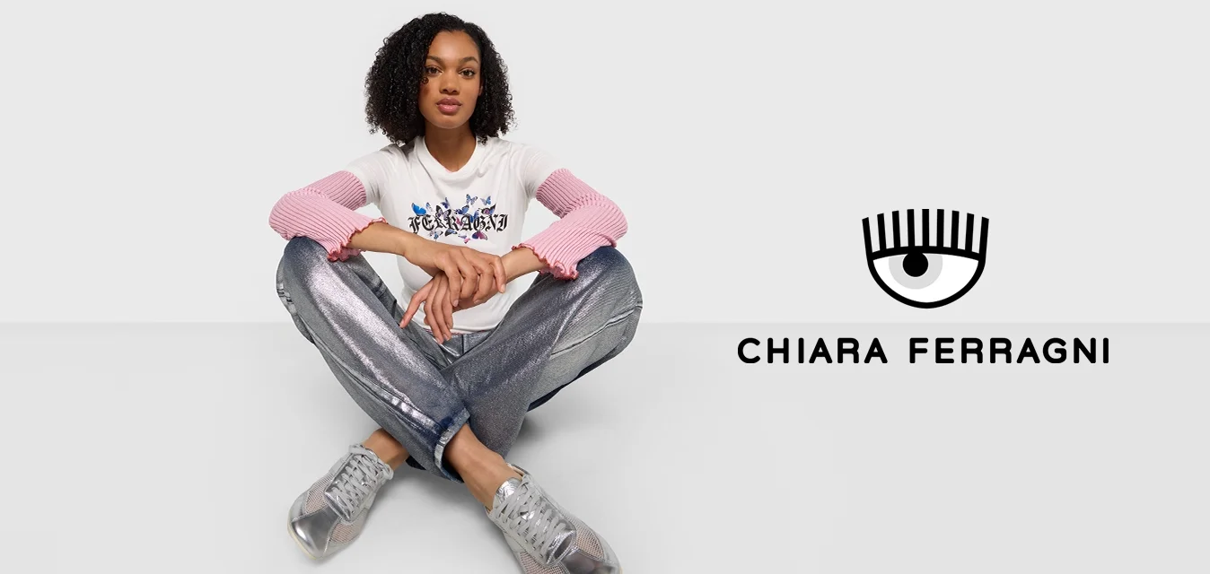 T-shirt bianca con maniche a coste rosa, dotata di una grafica, abbinata a pantaloni metallici argento e sneakers trasparenti, posata su uno sfondo bianco.