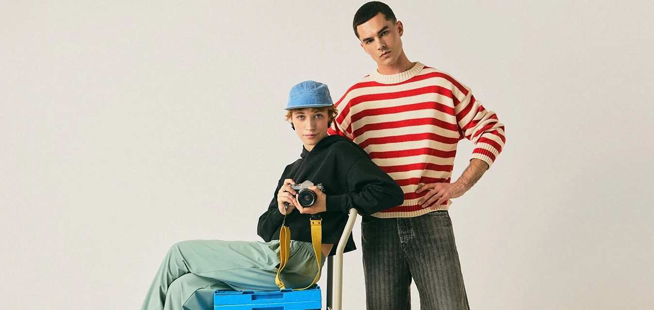 Carrello utility blu con ruote che trasporta una scatola di stoccaggio blu. Due persone posano accanto al carrello, una seduta e una in piedi, entrambe in abbigliamento casual.