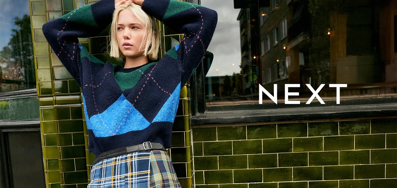 Maglione azzurro, verde e blu con fantasia, dalla vestibilità ampia, abbinato a una gonna a pieghe scozzese con dettagli gialli e una cintura nera.