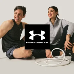 Due adulti in abbigliamento sportivo seduti per terra che sorridono, con una corda da esercizio bianca arrotolata tra di loro su uno sfondo neutro.