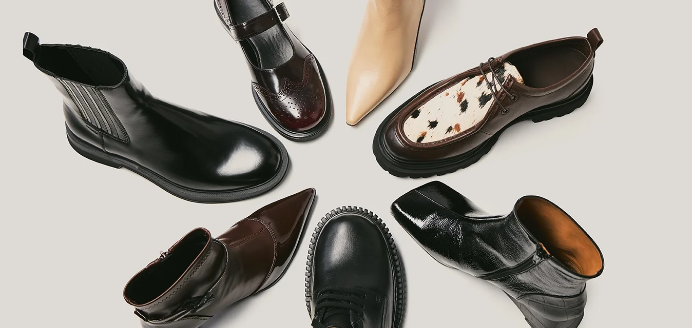 Sette paia di scarpe in vari stili: stivali alla caviglia in pelle nera e marrone, un stivale beige a punta e una scarpa marrone con un dettaglio maculato.