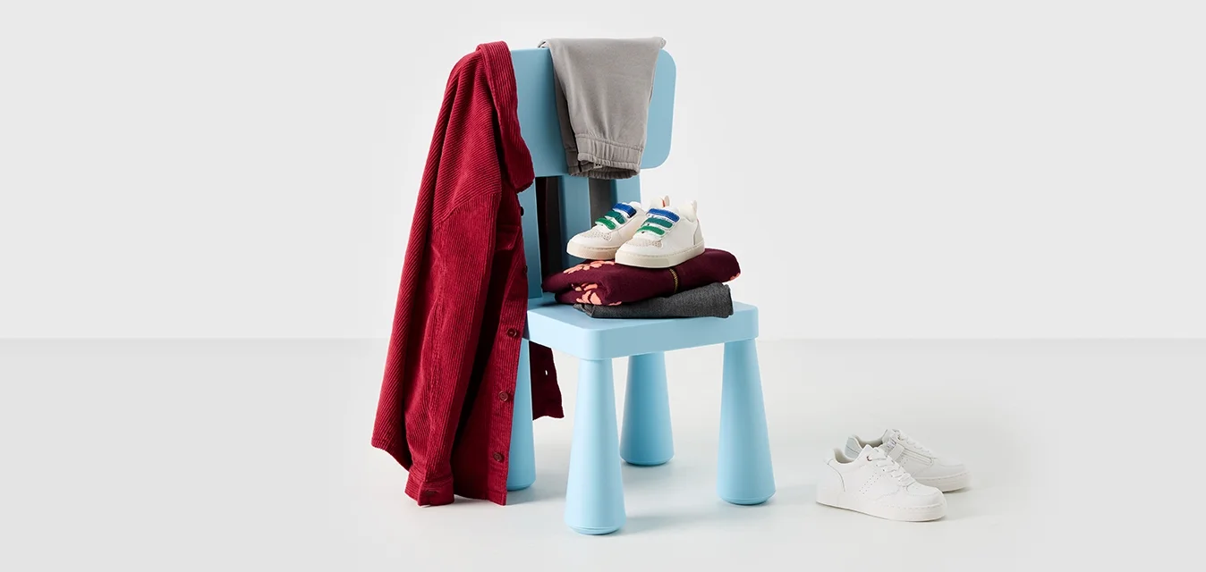 Sedia di plastica blu con una coperta rossa drappeggiata sopra, pantaloni grigi e due paia di scarpe - sneakers bianche e un paio bordeaux impilati sul sedile.