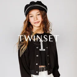 Giacca nera cropped con bottoni a pressione, indossata sopra una camicia nera con una lettera bianca. Gonna bianca svasata e un cappello nero con dettagli in catena.