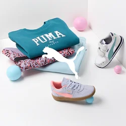 Felpa Puma in teal, leggings stampati in rosa e nero, e tre paia di scarpe da ginnastica in vari colori, sparse con palloni colorati.