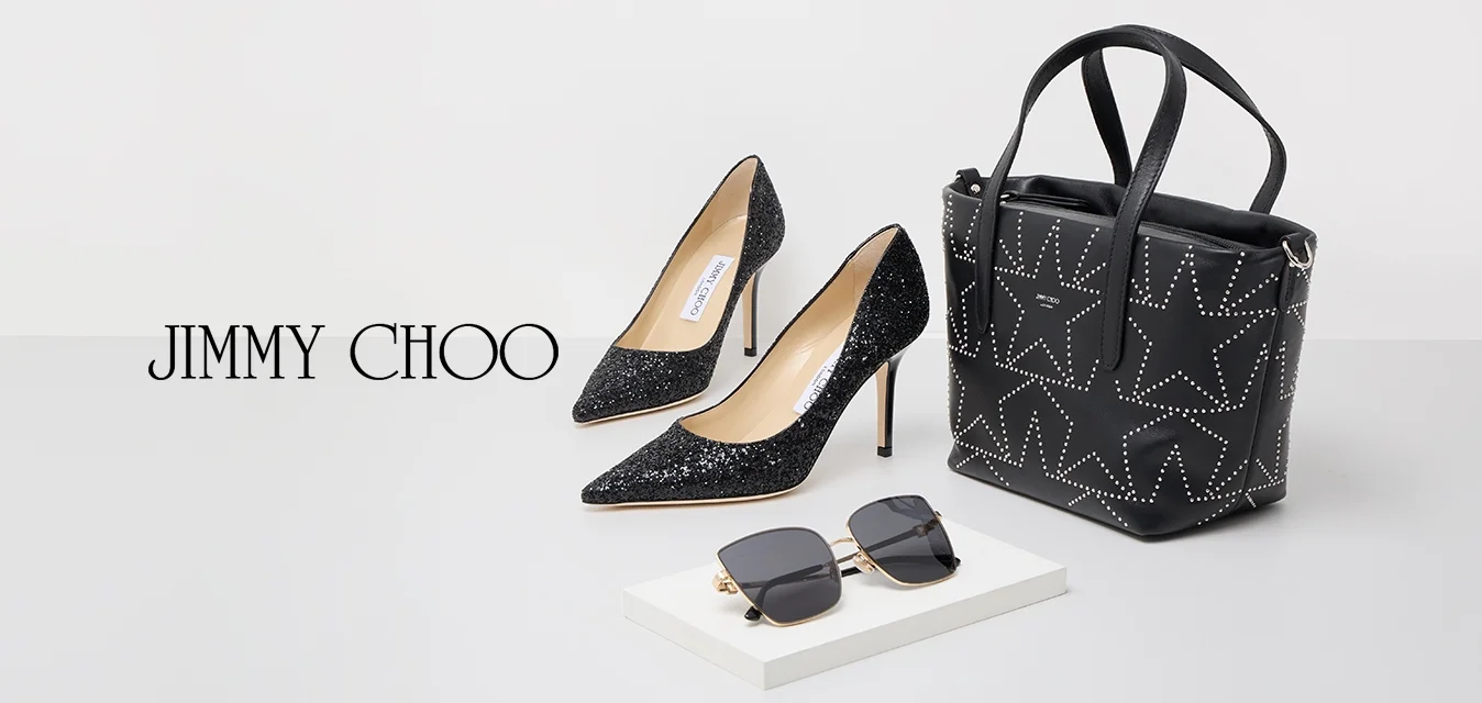 Scarpe nere con tacco alto e glitter, una borsa nera borchiata con motivi a stella e occhiali da sole oversize neri su una superficie bianca.