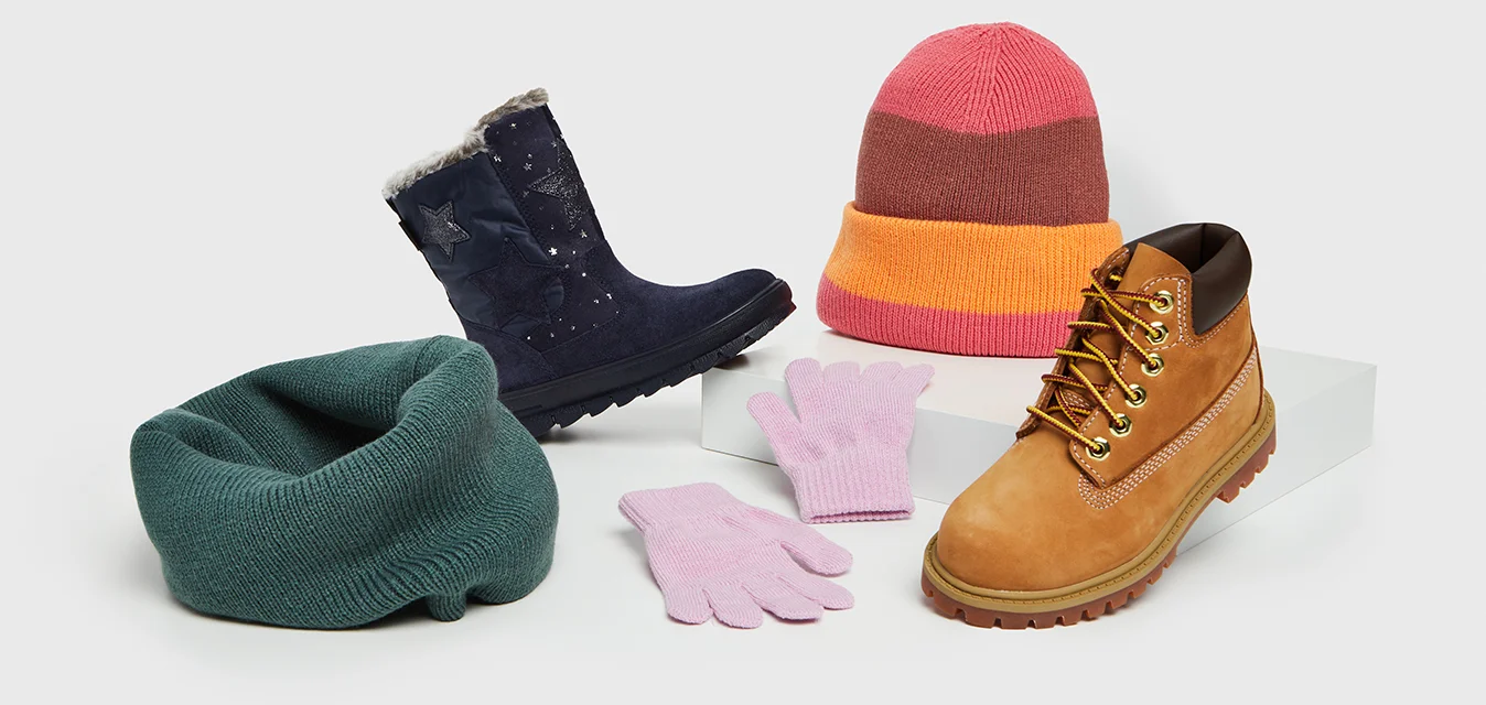 Calzature e accessori: stivali blu navy con bordino in pelliccia, sciarpa lavorata a maglia verde, guanti rosa, cappello a righe rosa e marrone, stivali tannati con lacci e dettagli dorati.