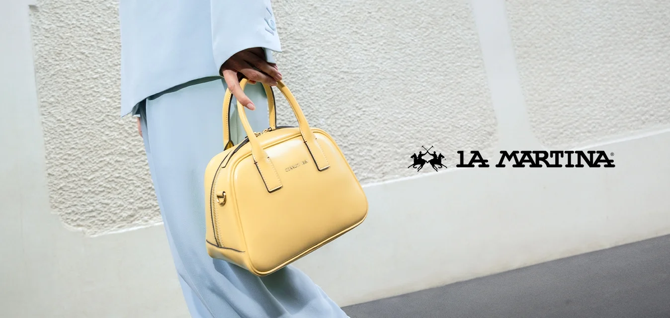 Borsa a tracolla in pelle gialla con forma arrotondata, doppie maniglie, chiusura a zip e una texture liscia. Indossata con un completo blu chiaro.