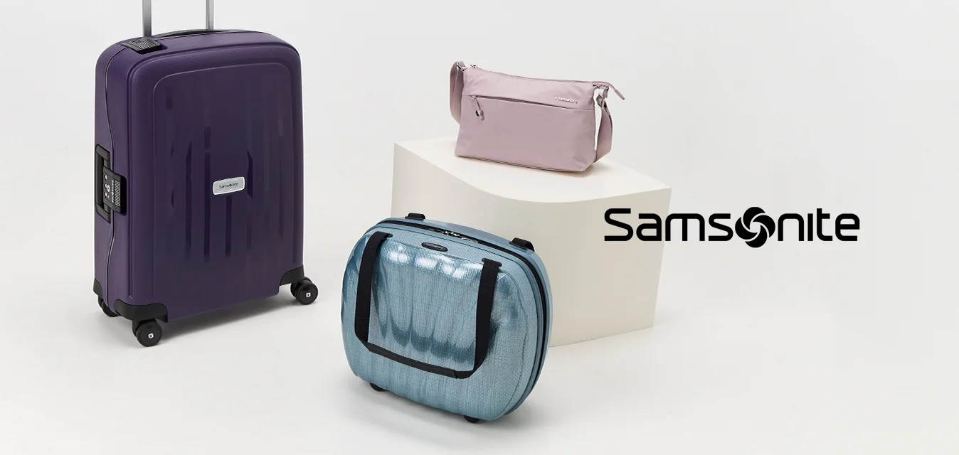 Tre pezzi di bagagli: una valigia viola con ruote, una borsa a mano blu e una pochette cosmetica rosa, esposti su una superficie bianca.