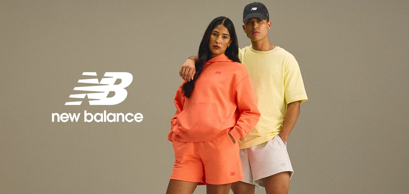 Due modelli stanno insieme, uno in una felpa arancione con cappuccio e pantaloni corti, l'altro in una maglietta gialla e pantaloni corti grigi. Entrambi indossano scarpe da ginnastica.