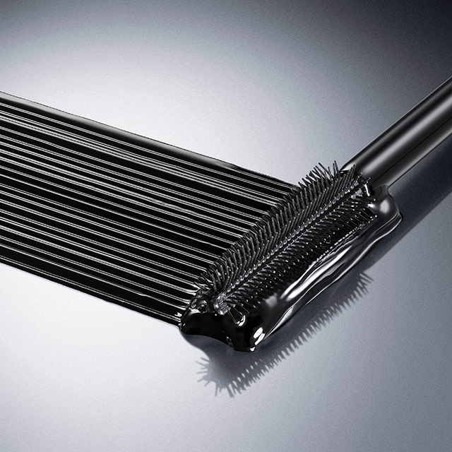 Un applicatore di mascara, con setole corte e fitte, crea pi&ugrave; strisce spesse e parallele di mascara nero su una superficie grigio chiaro lucida e riflettente.