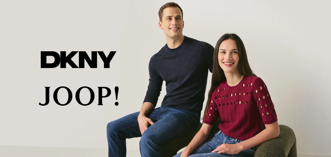 Giovane uomo con maglione nero e jeans e donna con top rosso e jeans decorati seduti su una sedia moderna con trama davanti a una parete bianca.