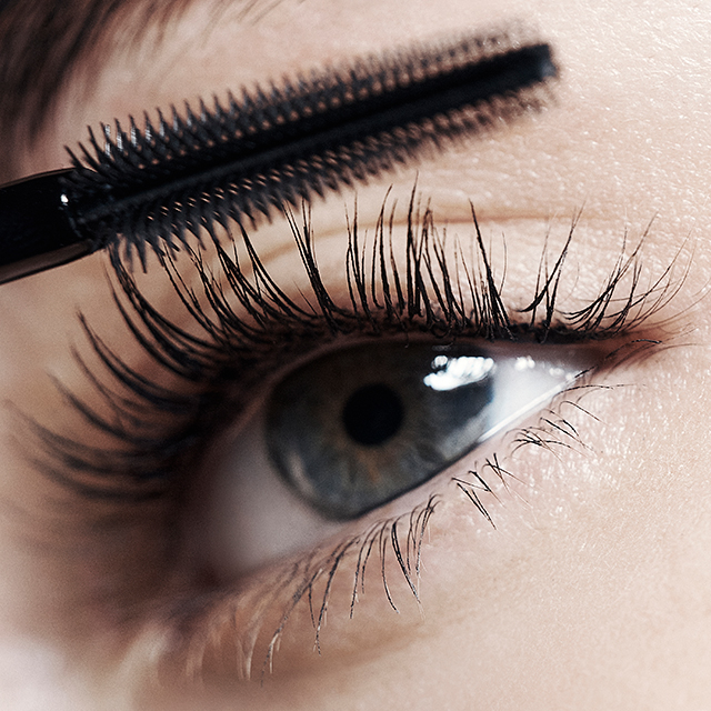 Un primo piano cattura un applicatore di mascara che applica il prodotto su un occhio con ciglia bellissime, evidenziando le ciglia scure e allungate sulla pelle chiara.