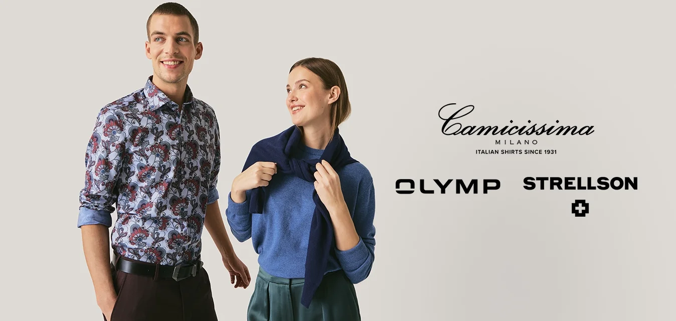 Giovane uomo e donna in piedi, sorridenti e guardando leggermente altrove; l'uomo indossa una camicia con motivi e la donna un maglione blu con sciarpa blu scuro.