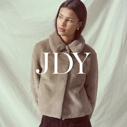 Giacca in pelliccia sintetica marrone con colletto rotondo, abbinata a una gonna in velluto a coste nera con bottoni frontali e due tasche. Sfondo crema.