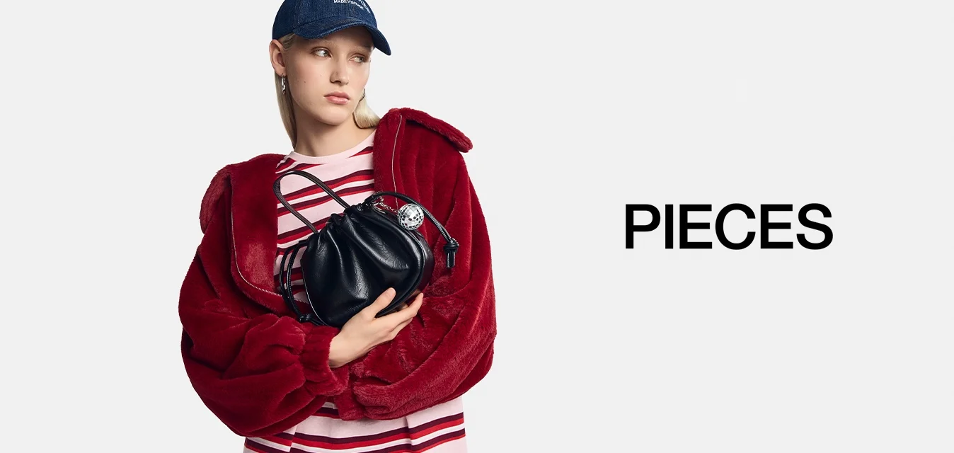 Borsa a tracolla in pelle nera con forma arrotondata e chiusura con cordoncino, appoggiata su una giacca in pelliccia sintetica rossa e una camicia a righe rosa e bianca.