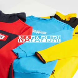 Tre maglioni esposti su una superficie bianca: rosso e nero, blu e giallo. Ognuno ha un marchio distintivo e colori contrastanti sui polsini.