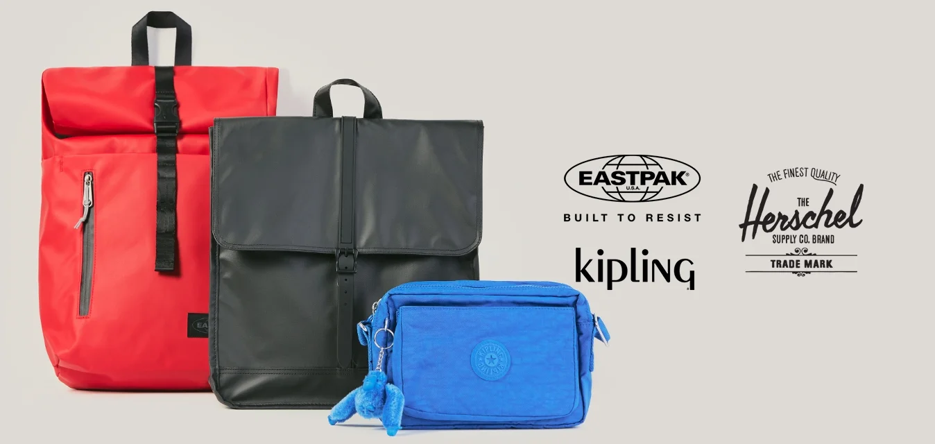 Tre zaini raggruppati: uno rosso alto con apertura a rotolo, uno nero medio con patta superiore e uno piccolo blu rettangolare con portachiavi.