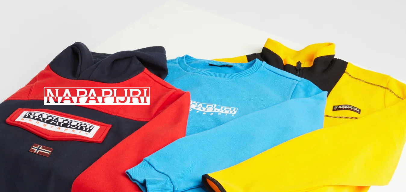 Tre maglioni esposti su una superficie bianca: rosso e nero, blu e giallo. Ognuno ha un marchio distintivo e colori contrastanti sui polsini.