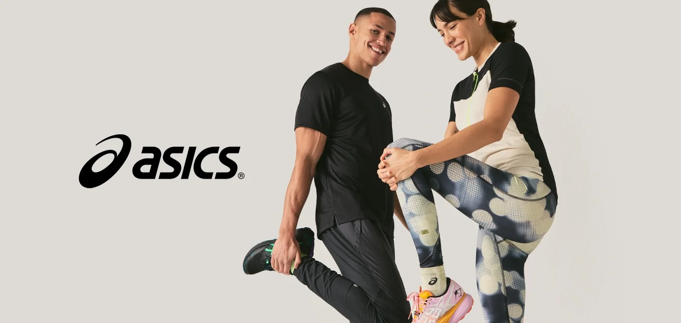 Uomo e donna in abbigliamento sportivo sorridenti mentre si allungano le gambe contro uno sfondo chiaro e uniforme.