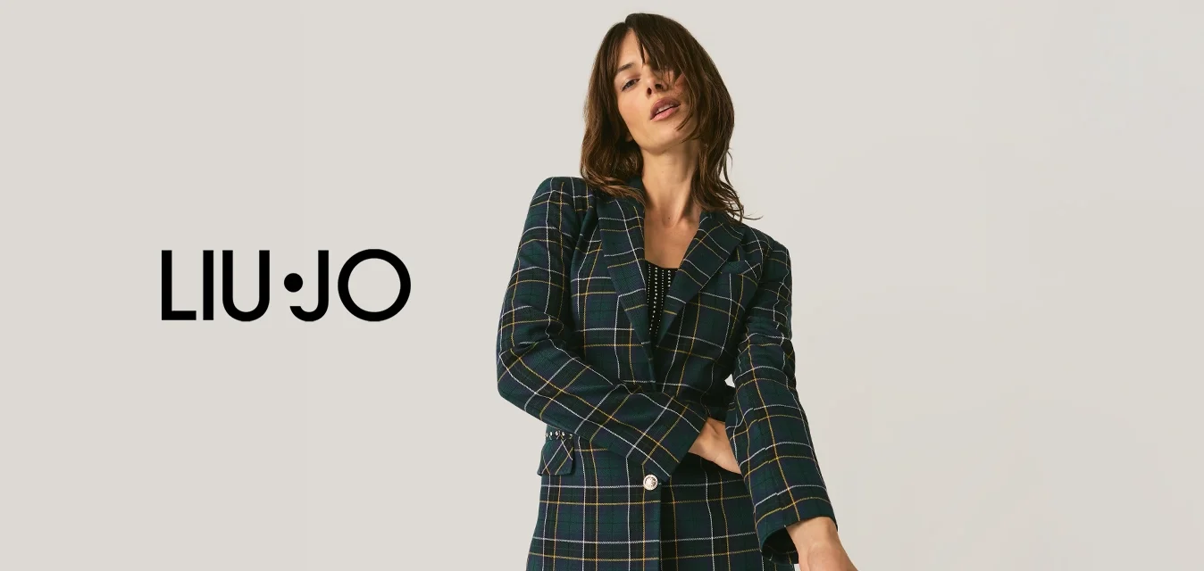 Donna in posa con un blazer a quadri e pantaloni neri con paillettes, su uno sfondo chiaro e uniforme.