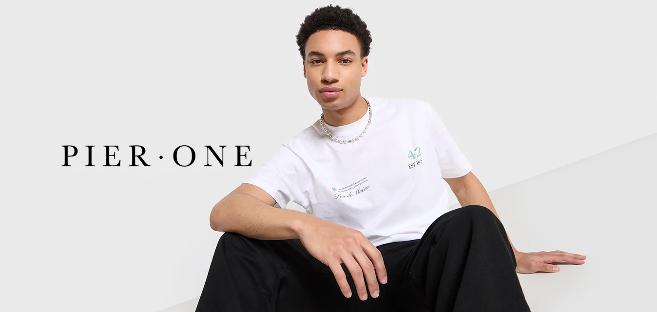 T-shirt bianco in cotone con testo e grafiche verdi; vestibilità rilassata. Indossato con pantaloni neri e una collana di perline argentate. Texture liscia.