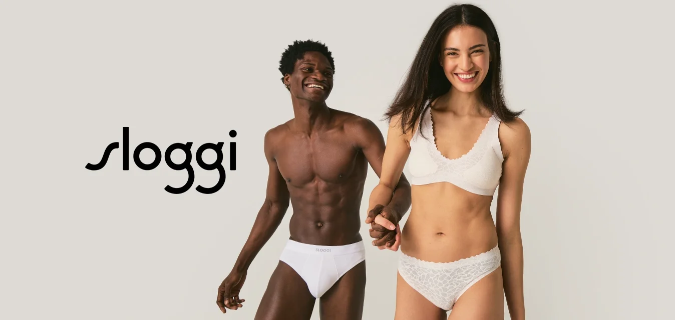 Giovane coppia sorridente che si tiene per mano, indossando biancheria intima bianca, in piedi contro uno sfondo chiaro e uniforme.