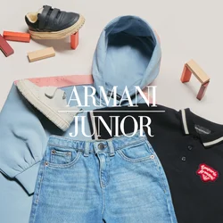 Felpa con cappuccio azzurro chiaro, polo nera con logo rosso, jeans blu e tre paia di scarpe da ginnastica colorate per bambini intorno ai vestiti su una superficie bianca.