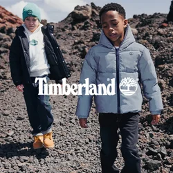 Due ragazzi con giacche invernali che camminano su un terreno roccioso con rocce vulcaniche sotto un cielo parzialmente nuvoloso.