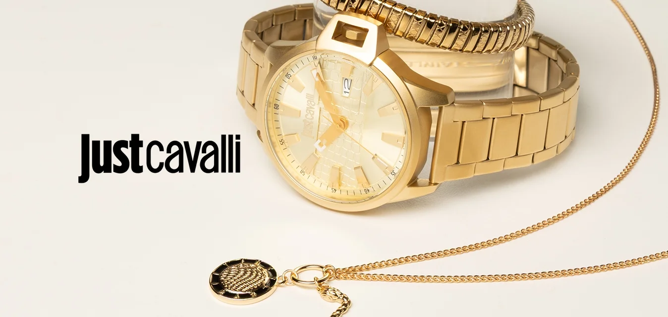 Due orologi d'oro impilati su un supporto trasparente e una delicata collana d'oro con un pendente circolare nero e oro su una superficie bianca.