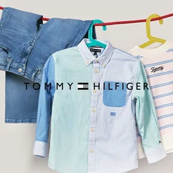 Camicia a righe blu e bianche con taschino blu, appesa accanto a un maglione a righe rosa chiaro e navy e jeans in denim blu.