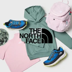 Felpa verde North Face, t-shirt rosa North Face, cappellino camouflage, zaino rosa e sneaker blu disposti su uno sfondo bianco.