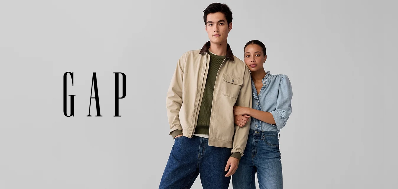 Giacca leggera beige, maglione verde, jeans a gamba larga in denim blu e scarpe beige. Donna con camicia blu e denim, scarpe marroni.