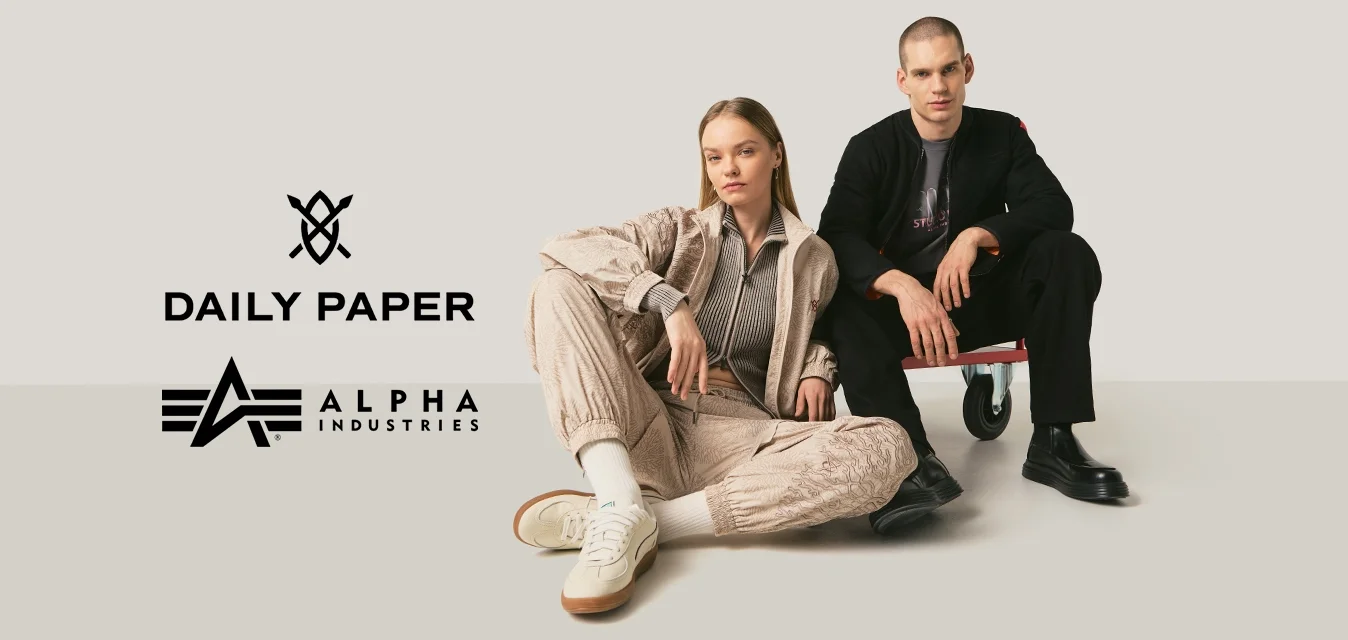 Giovane uomo e donna posano con abbigliamento casual da strada su uno sfondo neutro, la donna è seduta a terra, l'uomo su una piccola piattaforma con ruote.