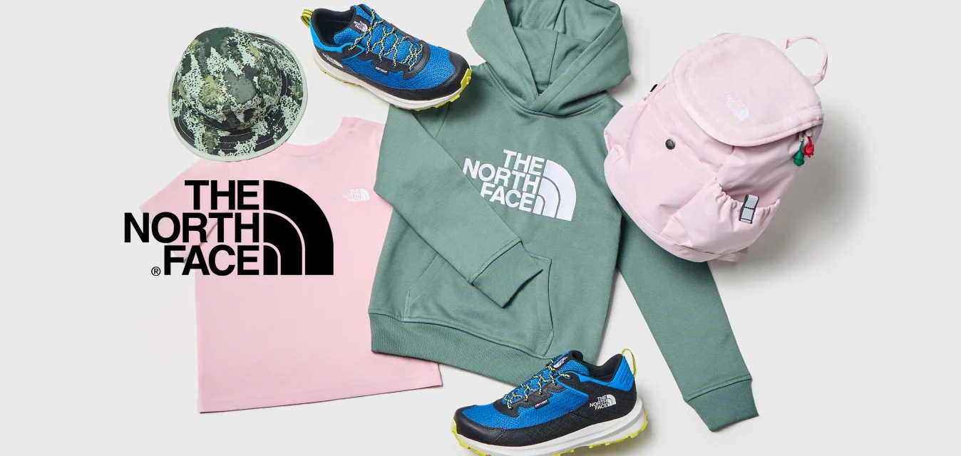 Felpa verde North Face, t-shirt rosa North Face, cappellino camouflage, zaino rosa e sneaker blu disposti su uno sfondo bianco.