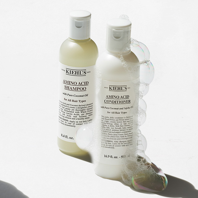 Flaconi di Amino Acid Shampoo e Amino Acid Conditioner di Kiehl&rsquo;s affiancati, con schiuma che avvolge il balsamo, su fondo bianco.