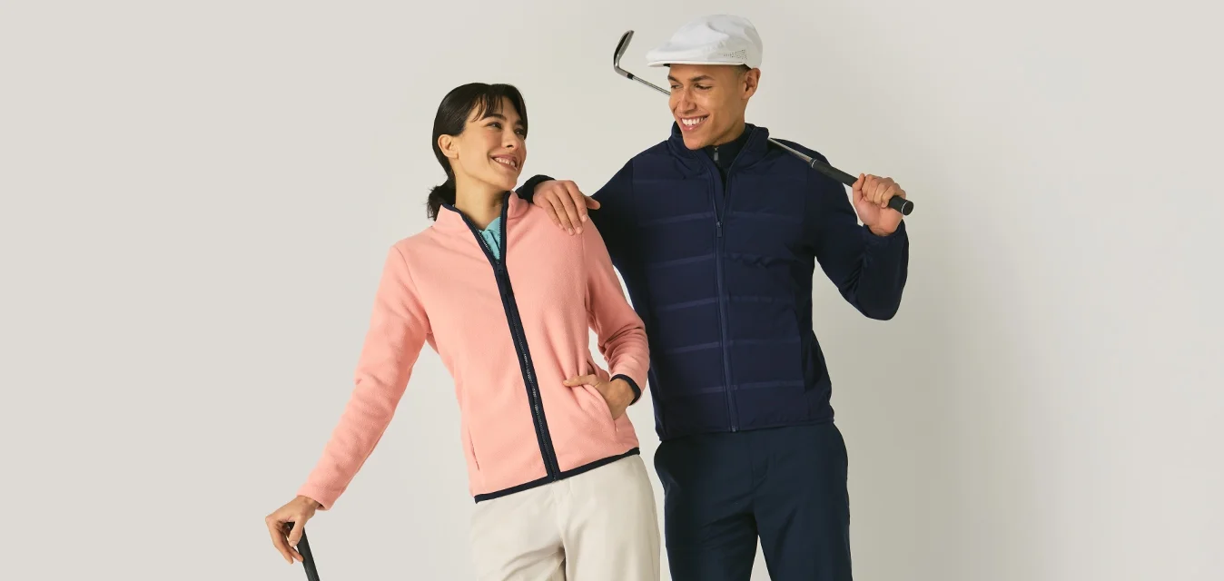 Due golfisti sorridenti, uno con giacca rosa appoggiato a una mazza, l'altro con giacca blu navy e cappellino che tiene una mazza sulla spalla.