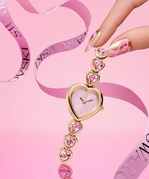 Dita che stanno per prendere un orologio con il quadrante a forma di cuore su sfondo rosa