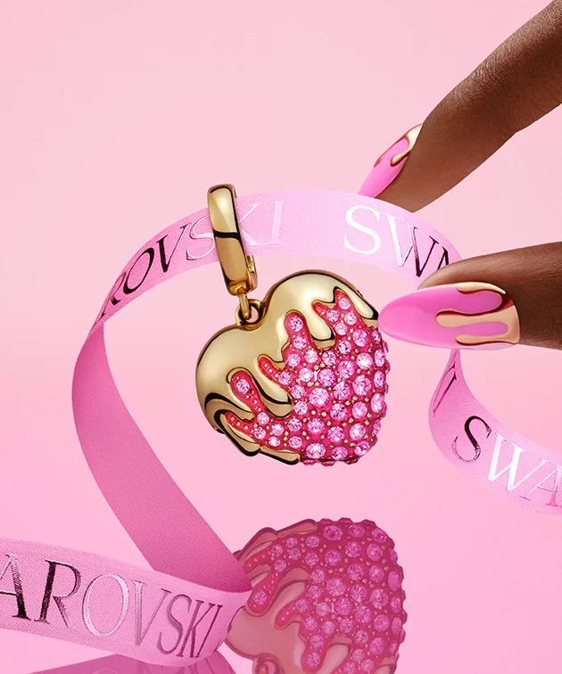 Dita che stanno per prendere un charm a forma di cuore su sfondo rosa