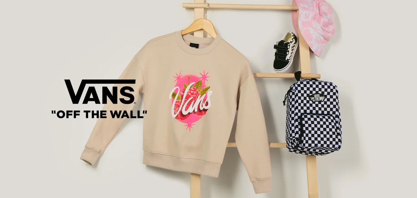 Felpa beige Vans, zaino a scacchi bianco e nero, cappello a secchiello rosa con fantasia e scarpe da neonato nere esposti su una scala di legno.