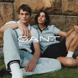 Due persone sono sedute contro un muro di pietra. L'uomo indossa una polo bianca e jeans chiari; la donna indossa una polo azzurra e pantaloni corti neri.