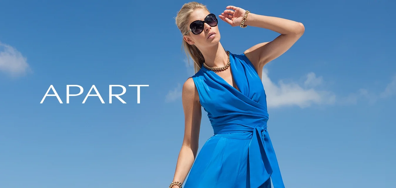 Giocattolo blu senza maniche con un design avvolgente, vita legata e gambe larghe. Tessuto liscio, abbinato a una collana d'oro e occhiali da sole.