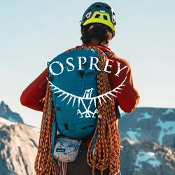 Zaino blu con superficie tessurizzata, corde da arrampicata arancioni attaccate, indossato su una maglietta a maniche lunghe arancione, contro uno sfondo montano.