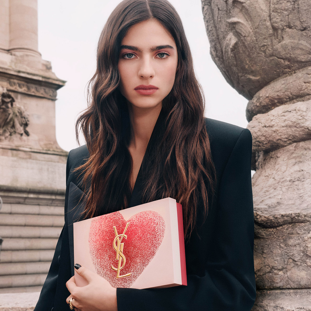 Una modella tiene una confezione regalo YSL rosa con un cuore rosso glitterato.