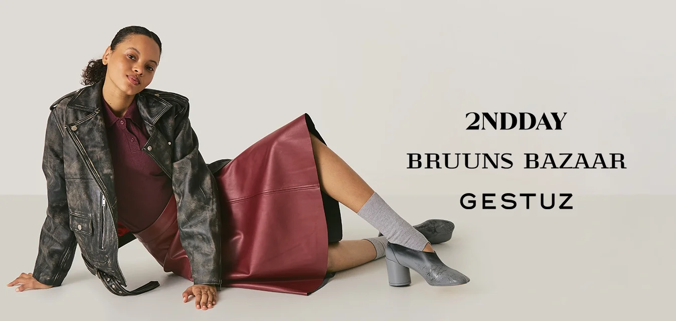 Donna sdraiata sul pavimento con una gonna di pelle bordeaux, giacca nera con motivo, calze grigie e scarpe con tacco largo argentate.