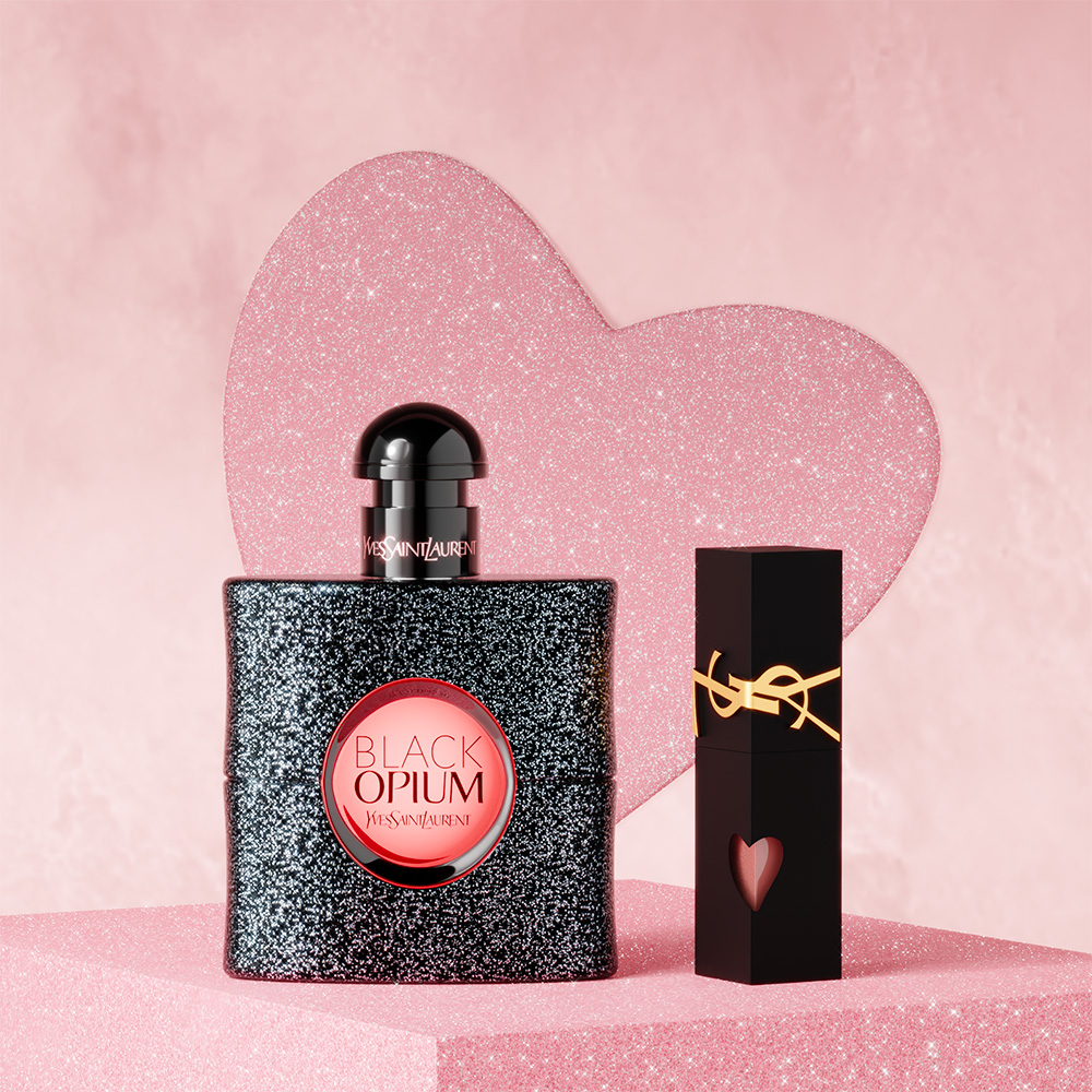 Un profumo YSL Black Opium e un rossetto nero sono esposti davanti a un cuore rosa scintillante.