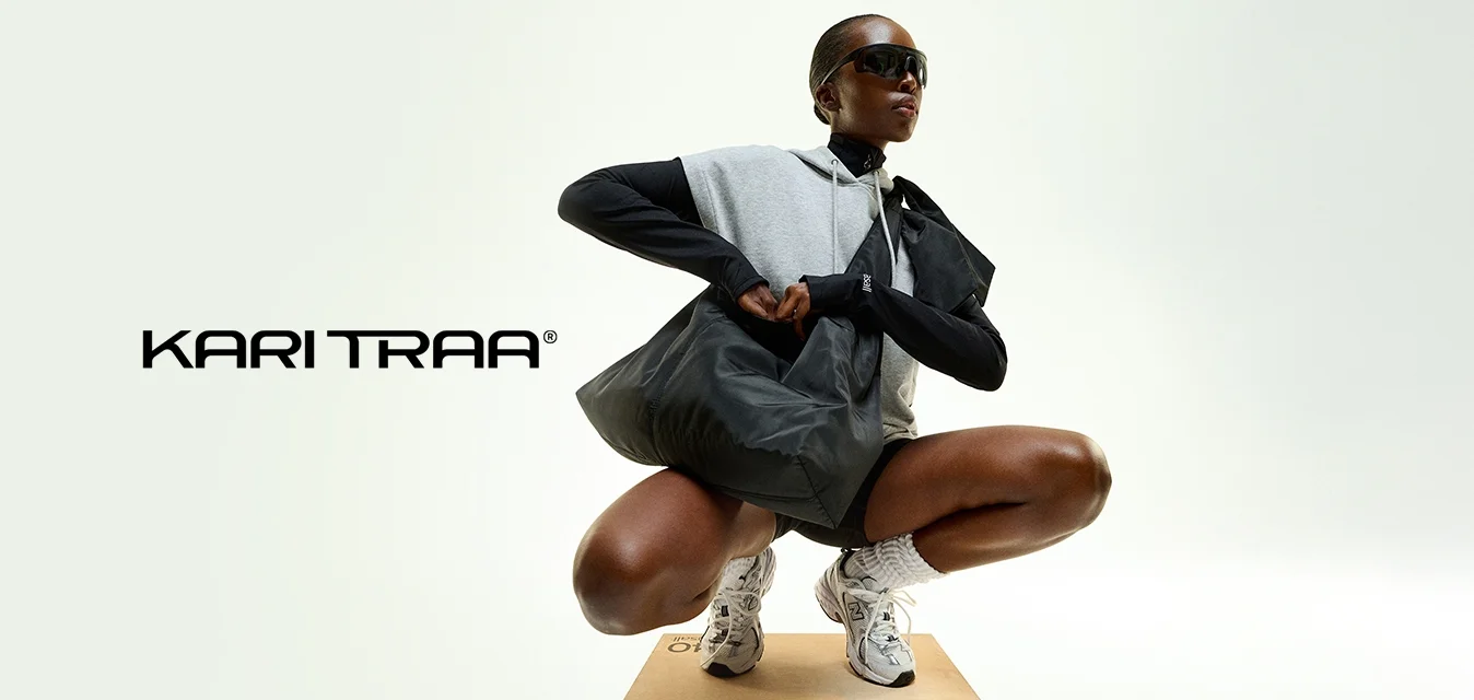 Persona sportiva accucciata su una cassa di legno che indossa occhiali da sole neri, felpa grigia senza maniche, maniche lunghe nere, scarpe da ginnastica bianche e tiene una grande borsa nera.