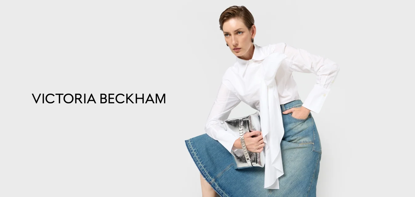 Camicia bianca con dettaglio annodato, abbinata a una gonna di jeans, accentuata da una borsa argentata e sandali neri con tacco alto.