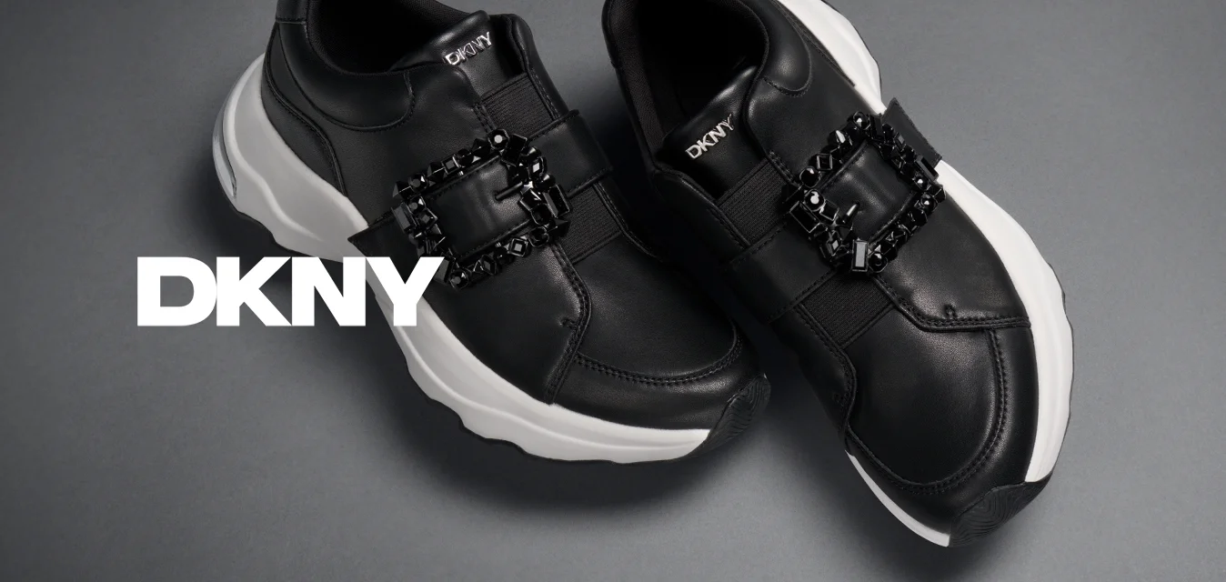 Sneakers neri senza lacci con suole bianche spesse e fibbie decorative in cristallo nero su sfondo grigio.