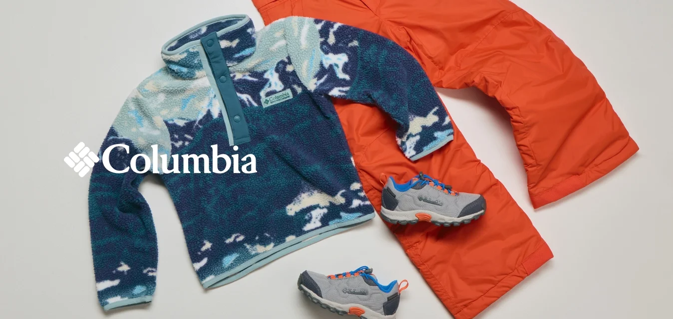 Pullover in pile con motivo blu e bianco, pantaloni isolanti arancioni brillanti e scarpe da trekking grigie con accenti blu e arancioni disposte su uno sfondo chiaro.